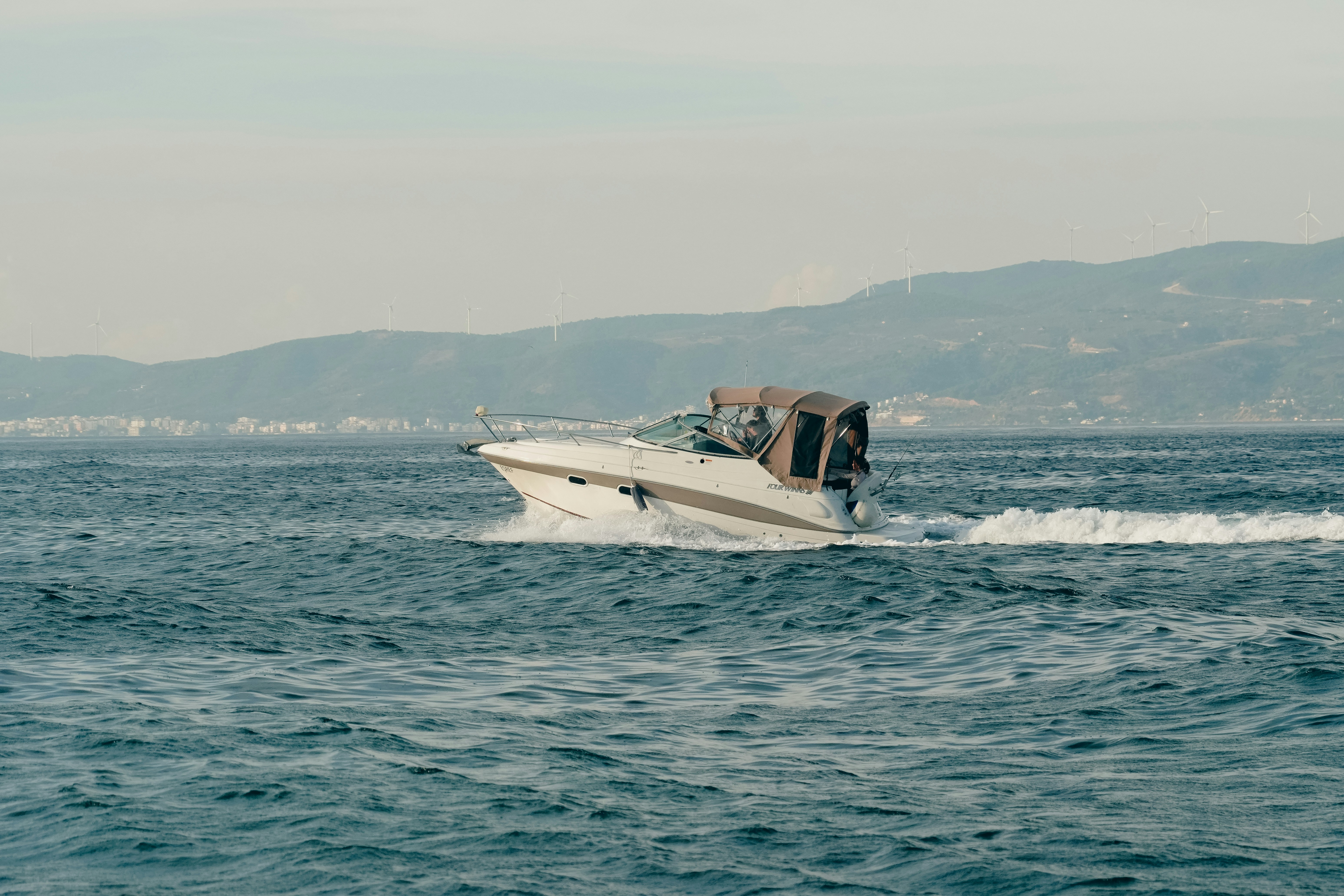 White motorboat crossing blue water near a mountainous coast